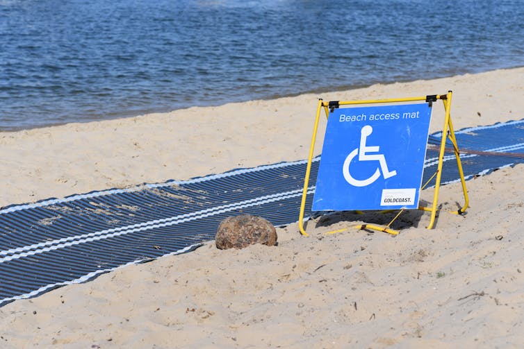 A long pathway mat on a beach with a disabled access sign.