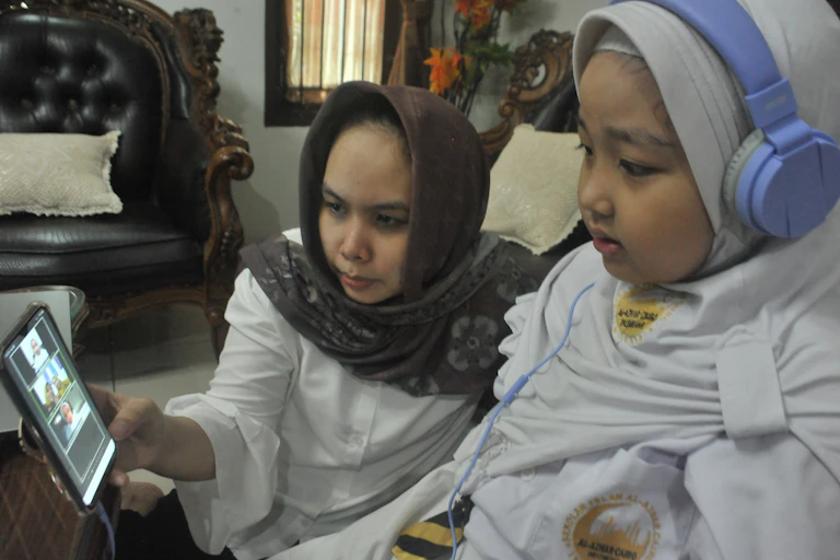 A parent accompany her child during an online learning session.