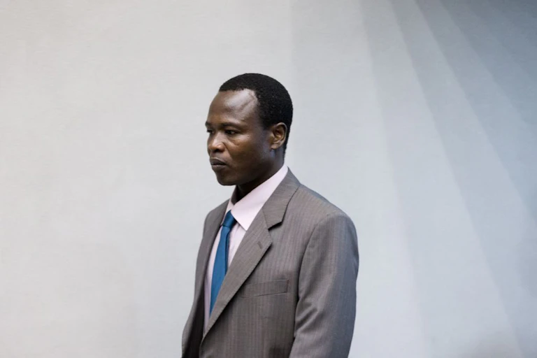 A man dressed in a suit and tie, against a plain background
