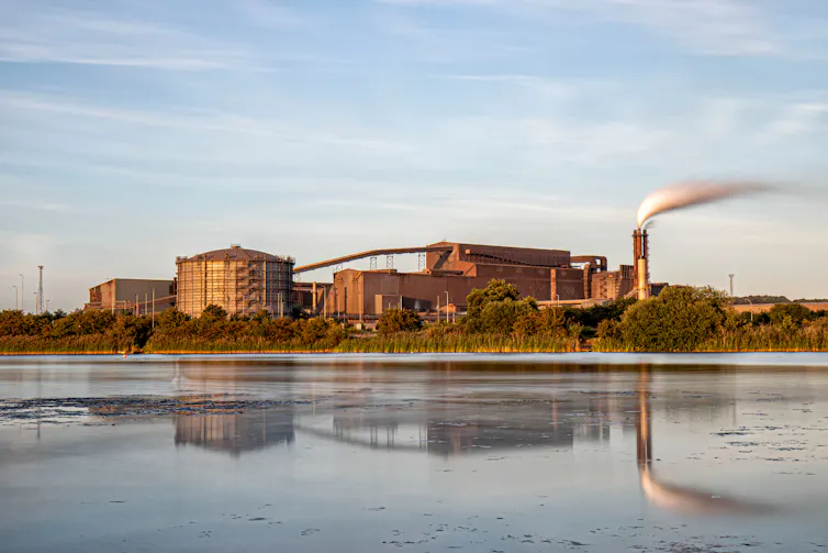 A mudflat with a large industrial complex in the background.