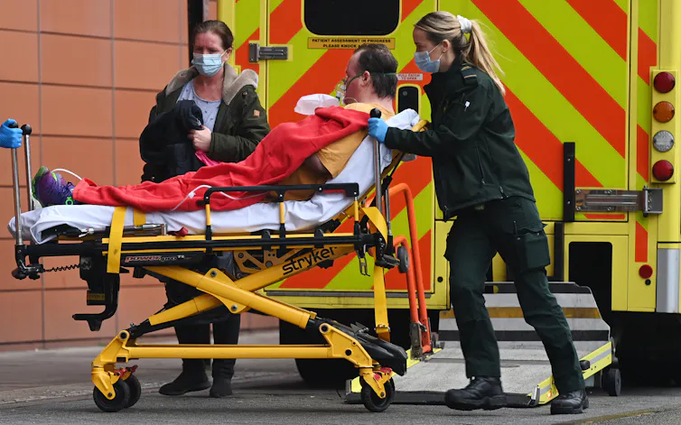 A man wearing on oxgen mask is wheeled into hospital by paramedics.