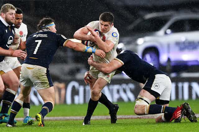 An England rugby player being tackled by Scotland players during a Six Nations match, February 2021.