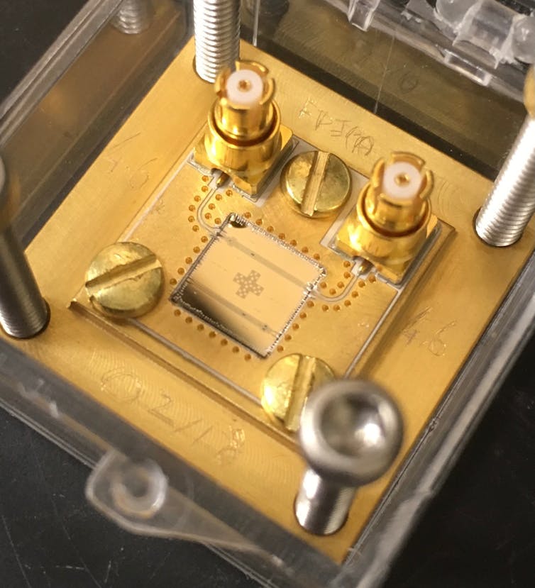A superconducting circuit, a small gold-colored square mounted onto a golden metal board.
