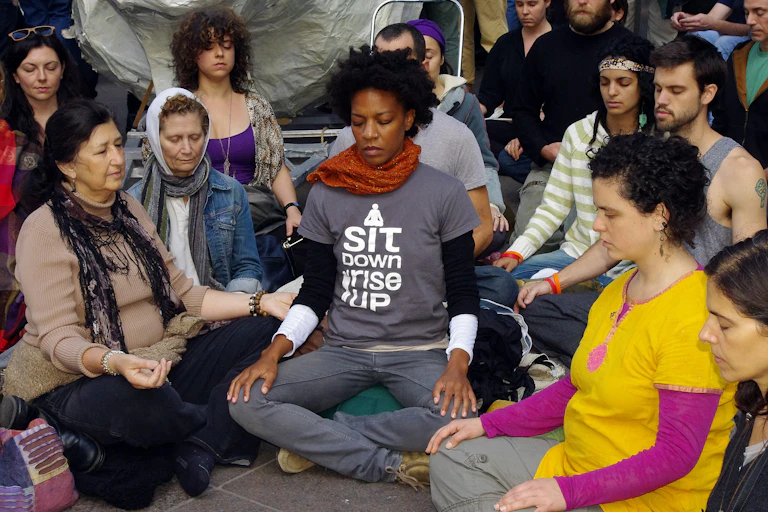 People sit on the ground and meditate. One t-shirt reads, "I sit down, I rise up.'