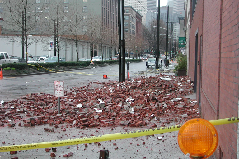 Rubble lies on a sidewalk in front of yellow police tape.