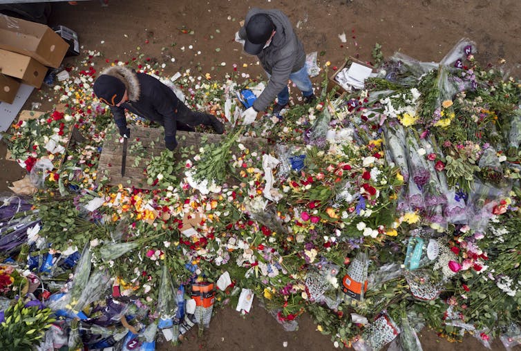 Overhead view of two people surrounded by flowers, chopping them up on a wooden table.