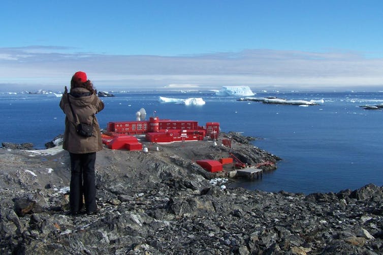 A person looking at the red research station in the distance, by the ocean