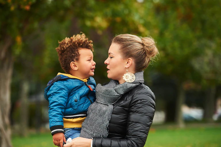 A young white mother holding her mixed-race toddler in her arms..