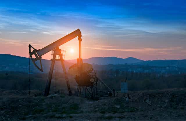 An oil derrick in a rocky field at sunset.