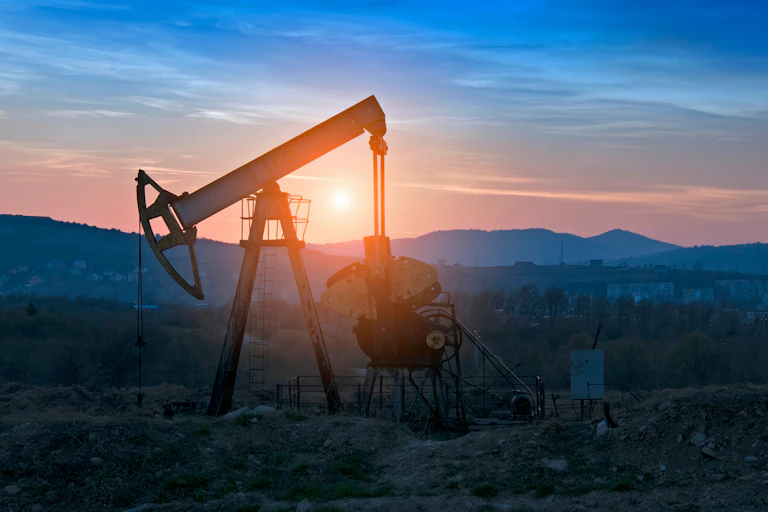 An oil derrick in a rocky field at sunset.