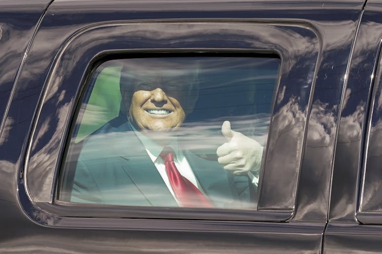 Trump smiles and gives the thumb's up from the back of a limo.