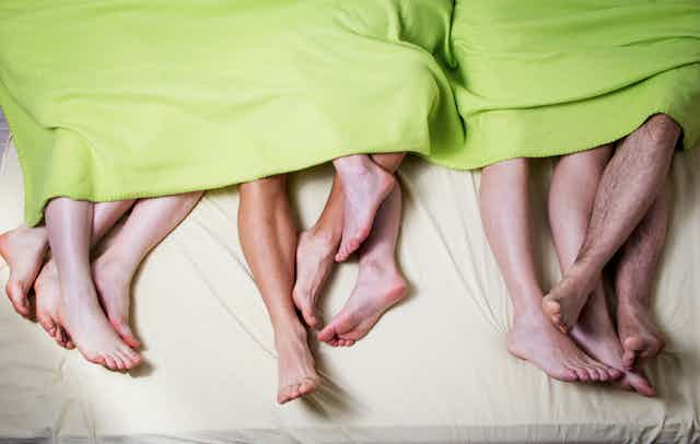 Six pairs of feet stick out from under a blanket.