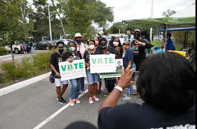 Several African American women pose for a photo while holding 'vote' signs.