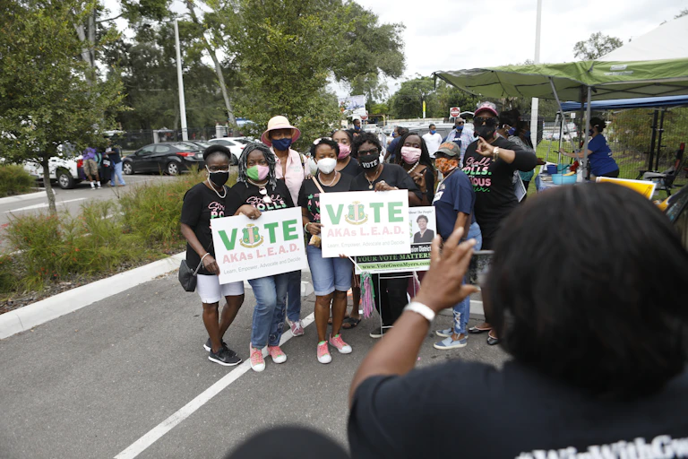 Several African American women pose for a photo while holding 'vote' signs.