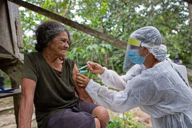 A Brazilian health worker administers a COVID-19 vaccine to an elderly woman.