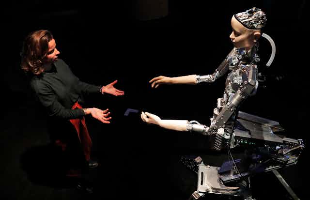 A woman and a humanoid robot reach out to each other
