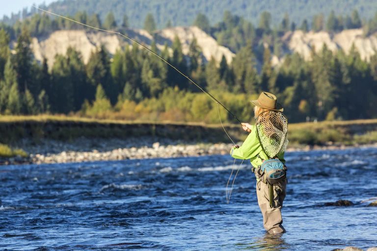 Woman with fly rod and net fishing in a stream