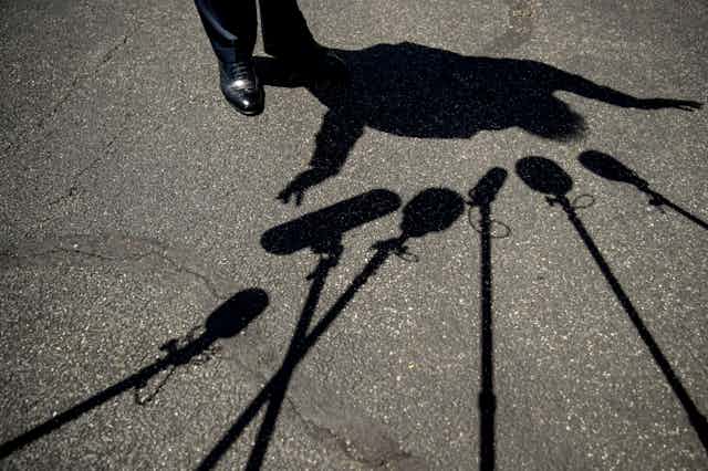 Trump's feet and his silhouette are seen surrounded by the shadows of microphones on asphalt.