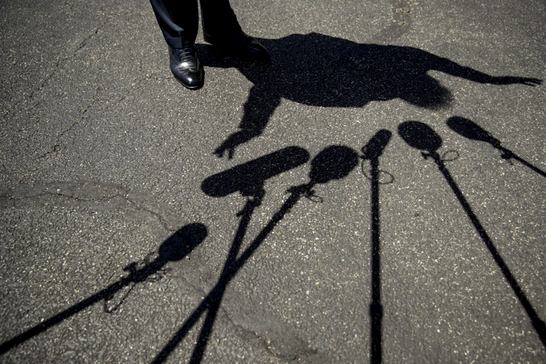 Trump's feet and his silhouette are seen surrounded by the shadows of microphones on asphalt.