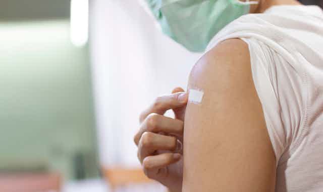 Young male wearing mask pointing to bandaid on upper arm