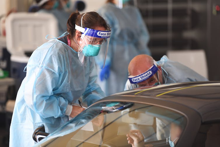 Two health-care workers conducting COVID testing at a drive-through site.