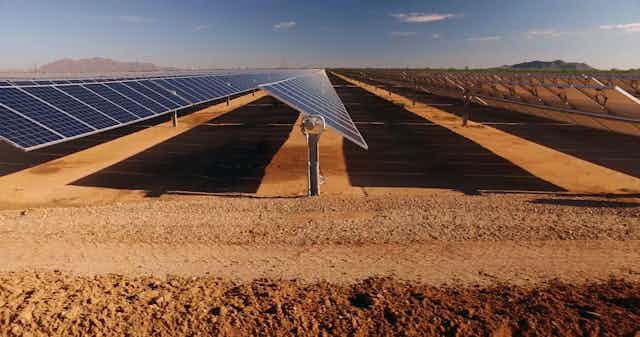 Three rows of solar panels in a desert viewed from the side.