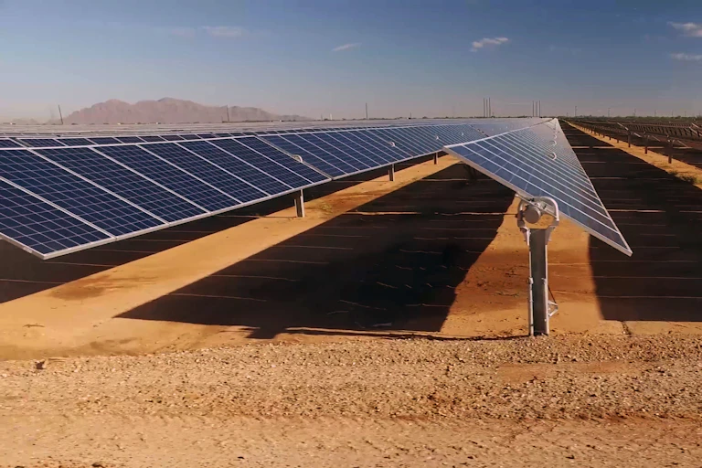 Three rows of solar panels in a desert viewed from the side.