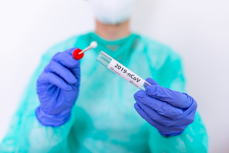 Someone in scrubs with gloves on holding a test tube and cotton bud.