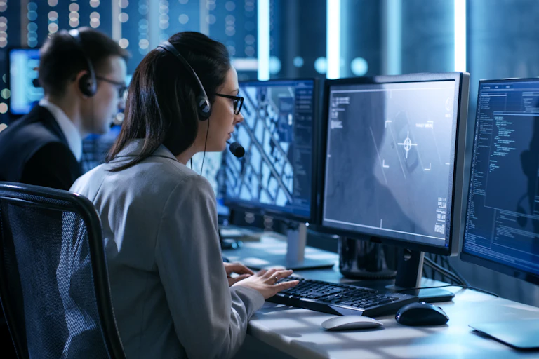 A man and a woman with headsets monitor communications on computer screens