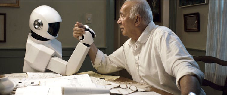 A robot and an elderly man arm wrestle on a table