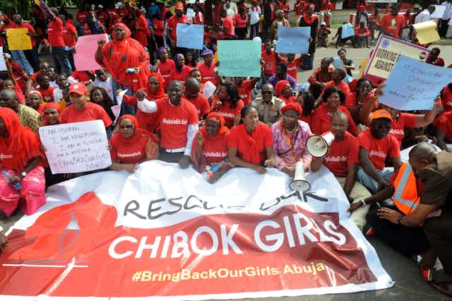 A group of people wearing red shirts and holding a large printed banner while protesting on the street of Abuja, Nigeria. 