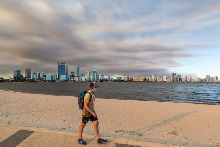 A man wearing a mask walks along a beach in Perth.