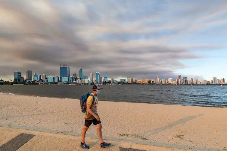 A man wearing a mask walks along a beach in Perth.