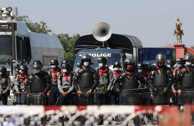 Myanmar police with security vehicles at a barricade to hold back protestors.