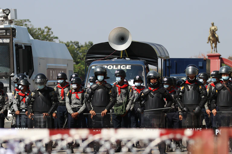 Myanmar police with security vehicles at a barricade to hold back protestors.