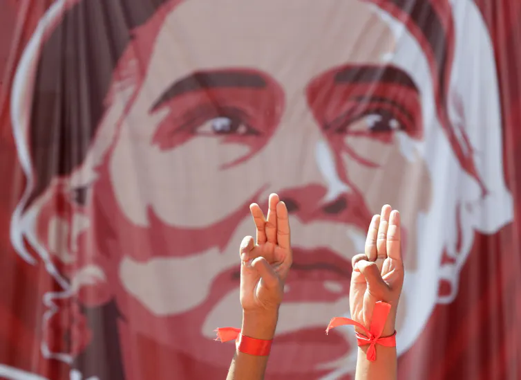 Poster of Aung San Suu Kyi with three-fingered salute of protester defiance in the foreground.
