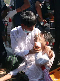 Person wearing white shirt and face mask hold another lying down with wet hair