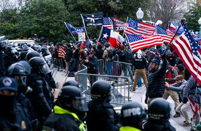 Trump supporters waving American flags and Trump signs confront a line of police.