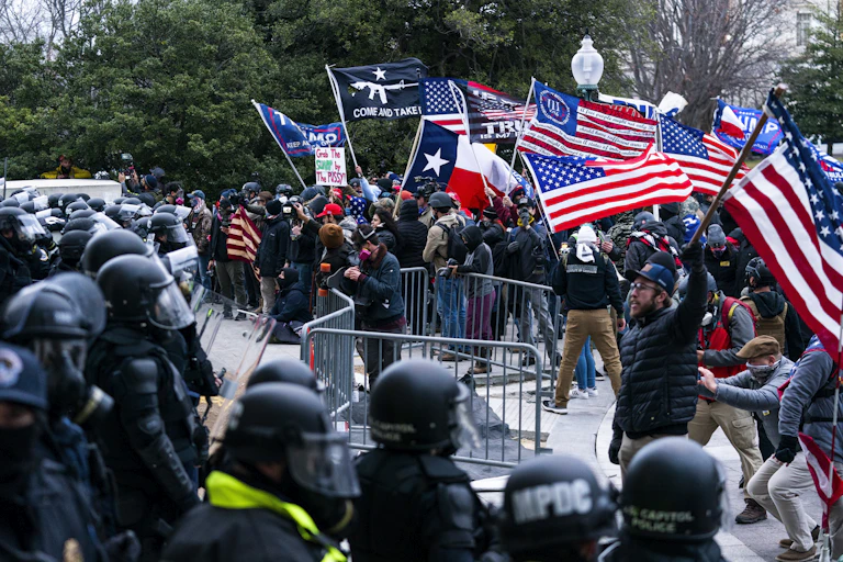 Trump supporters waving American flags and Trump signs confront a line of police.