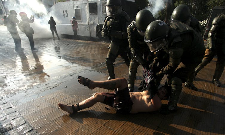 A man lies on the ground as police in riot gear surround him.
