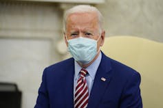 Biden wears a mask while sitting in the Oval Office.
