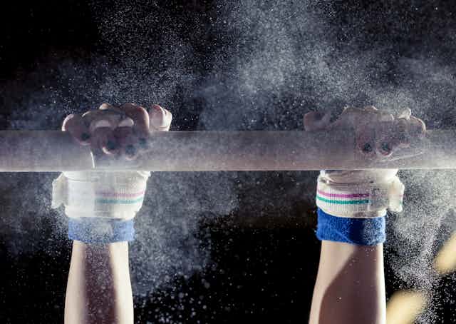 gymnast's hands on a bar with powder flying
