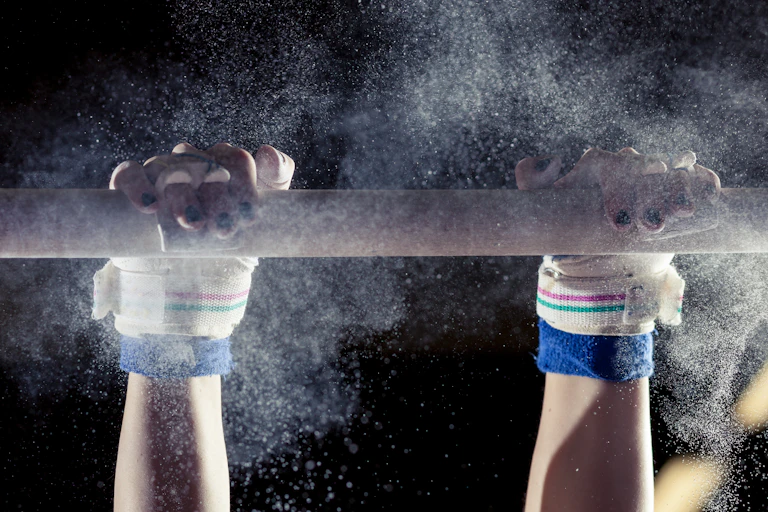 gymnast's hands on a bar with powder flying