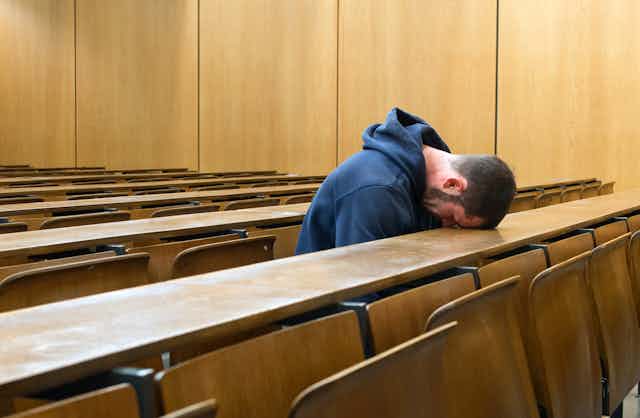 Lone student in lecture theatre with head on desk