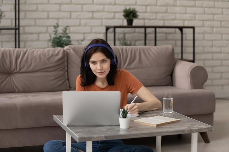 young woman takes notes as she sits in front of a laptop at home