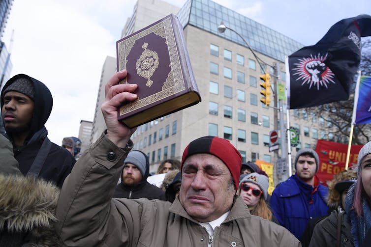 A Muslim man at a rally holding up a copy of the Quran and crying
