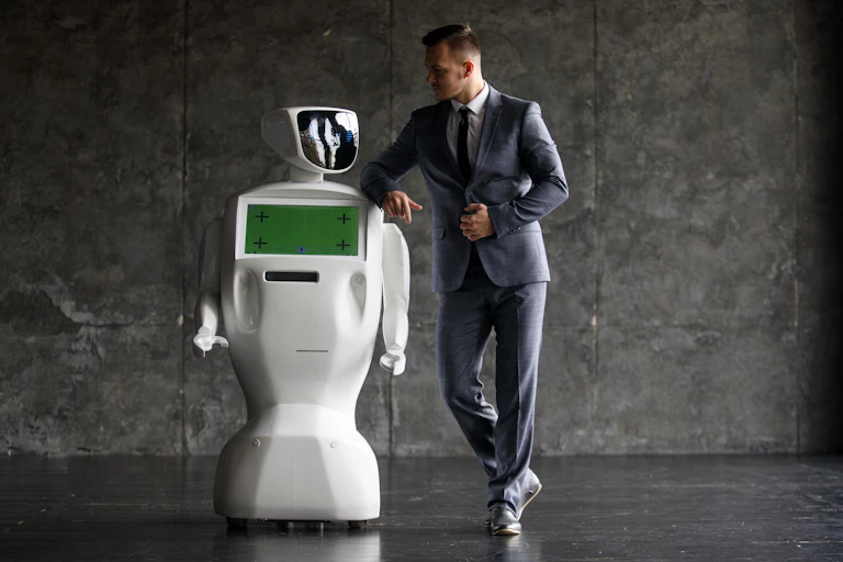 A man in a suit leans casually on the shoulder of a basic-looking robot