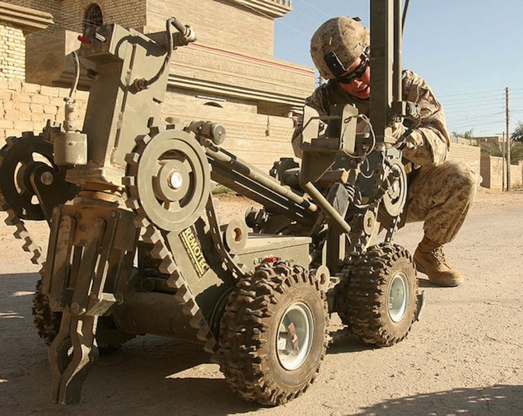 A robot on wheels is attended to by a soldier in combat gear