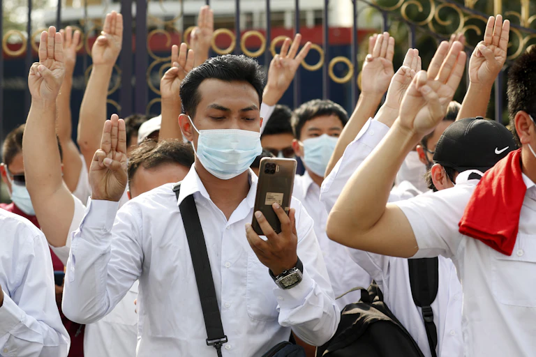 Group of young men and women in white shorts and COVID masks with their left hands using three-fingered protest salute from The Hunger Games.