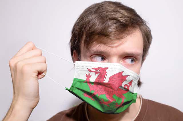 A man putting on a covid facemask bearing a Welsh flag design.